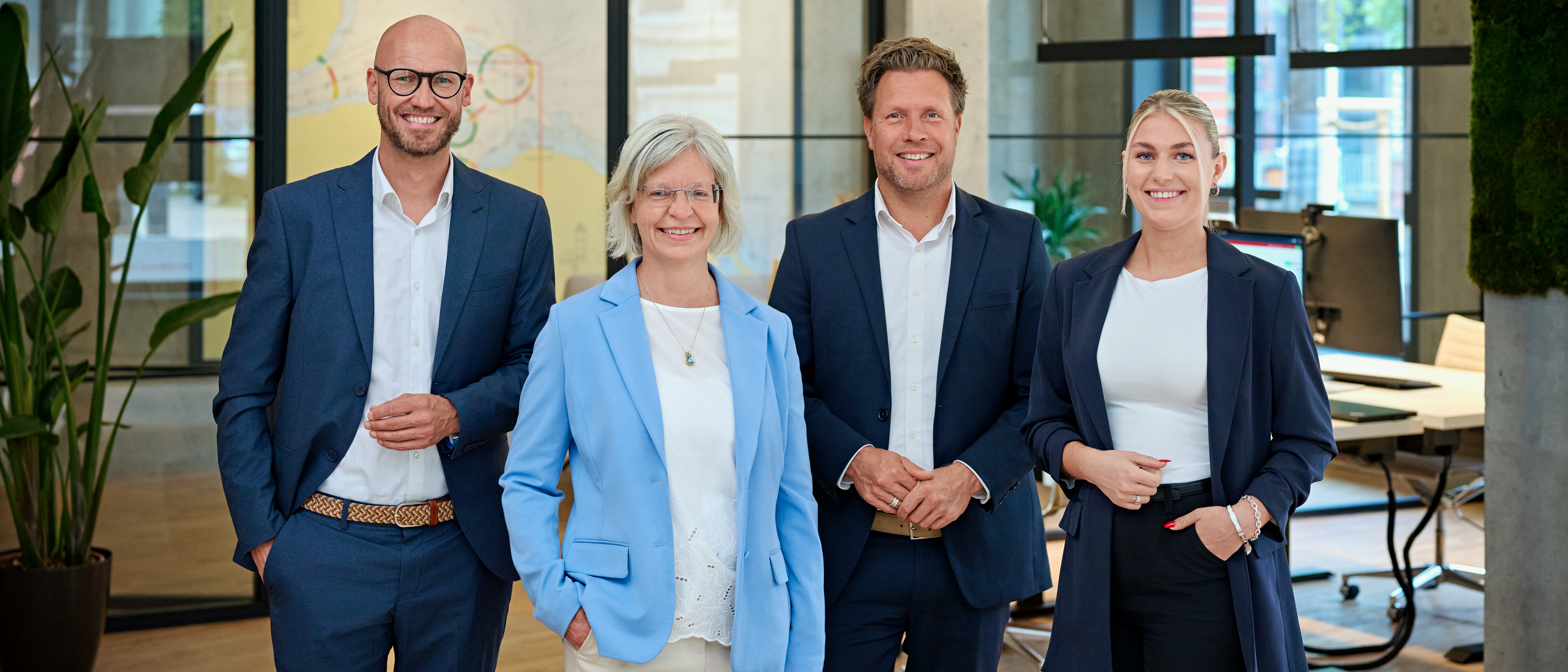 Vier Mitarbeiter von Toplage Immobilien in ihrem Büro an der Kieler Hörn, von links nach rechts: Geschäftsführer Jan Wohlert, Wiebke Zauka, Geschäftsführer Jan Marin, Marisa Lebert, alle in Businesskleidung. Im Hintergrund ist das Büro mit Schreibtischen zu erkennen.