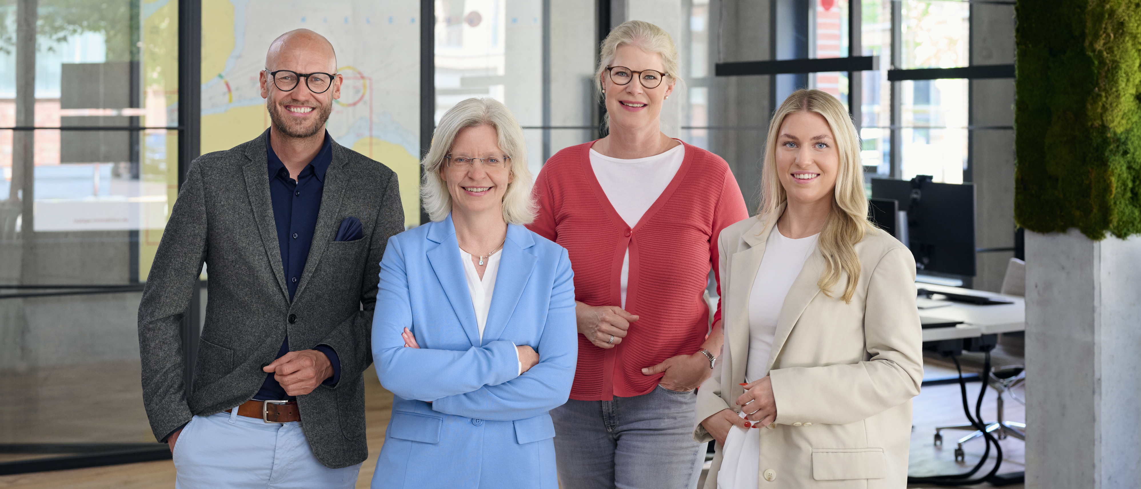 Vier Mitarbeiter von Toplage Immobilien in ihrem Büro an der Kieler Hörn, von links nach rechts: Geschäftsführer Jan Wohlert, Wiebke Zauka, Geschäftsführerin Sophie Hergst, Marisa Lebert, alle in Businesskleidung. Im Hintergrund ist das Büro mit Schreibtischen zu erkennen.
